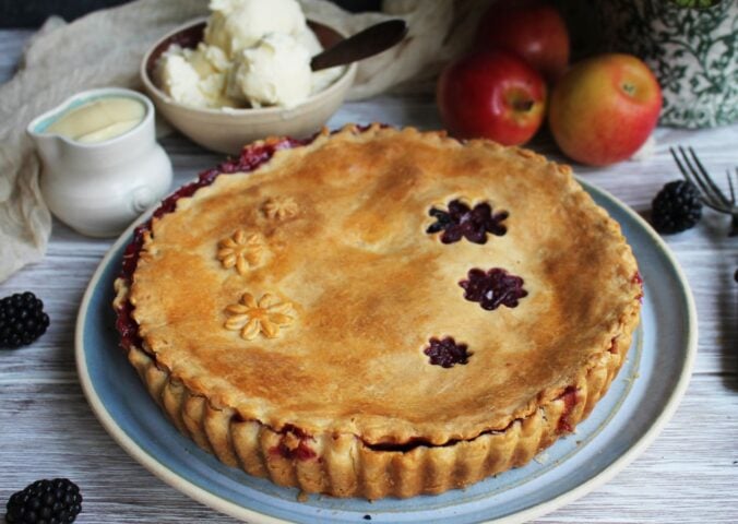 A vegan apple and blackberry pie next to some dairy-free cream and ice cream