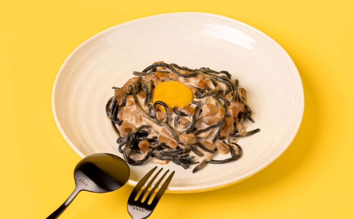 a bowl of charcoal spaghetti carbonara with vegan egg yolk and mushroom pancetta