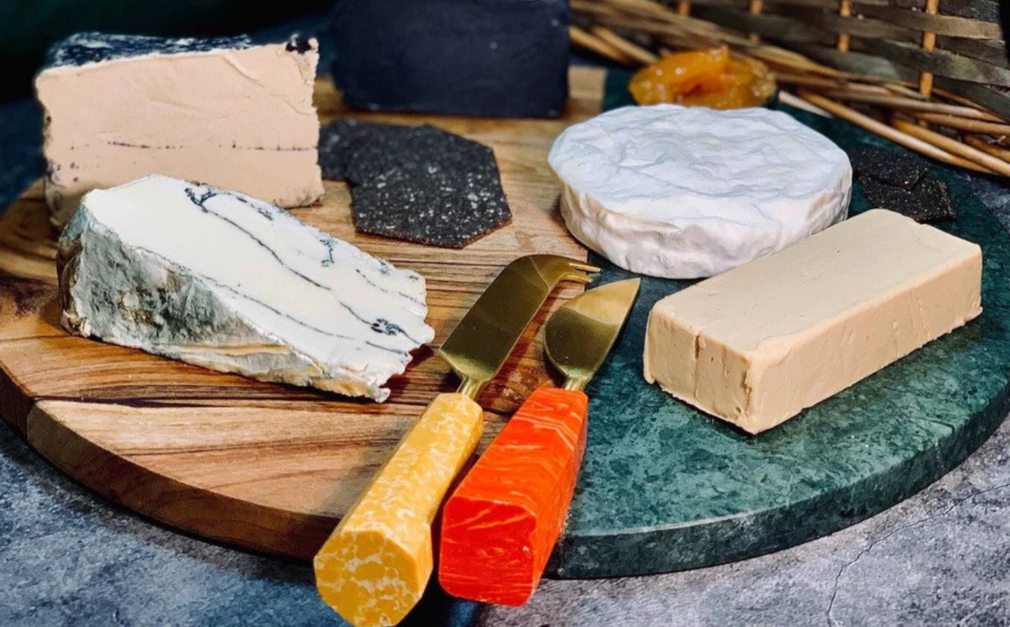 A selection of vegan dairy-free cheeses from la Fauxmagerie on a wooden and resin board with appropriate knives