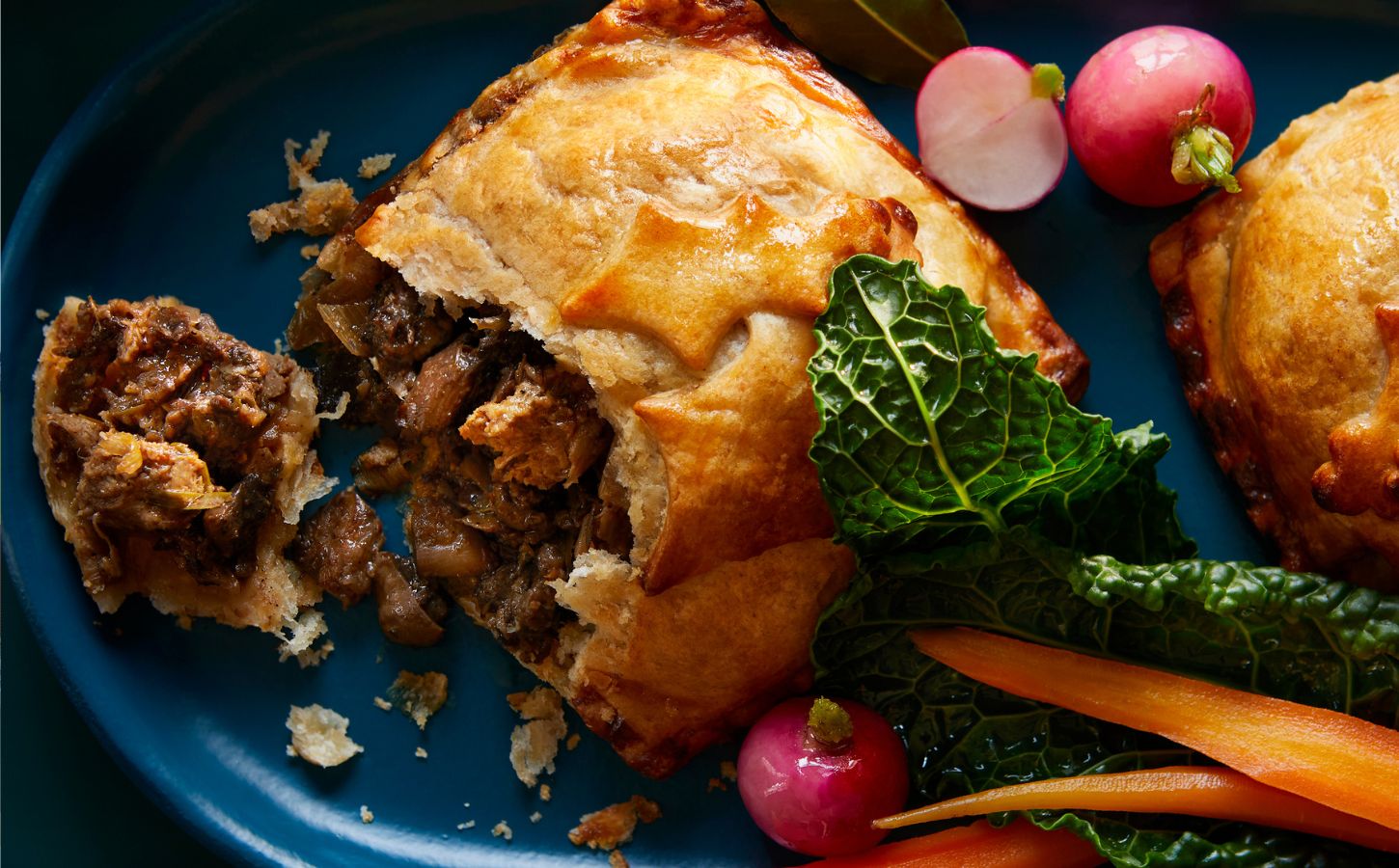 A vegan beef wellington from UK supermaret Waitrose. It's positioned on a plate next to radishes, cabbage, and carrots. the Wellington is part of Waitrose's 2023 Christmas range