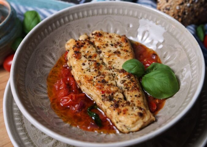 Photo shows two fillets of the latest Revo Foods product, vegan black cod, in a dish with a tomato-based sauce and green garnish