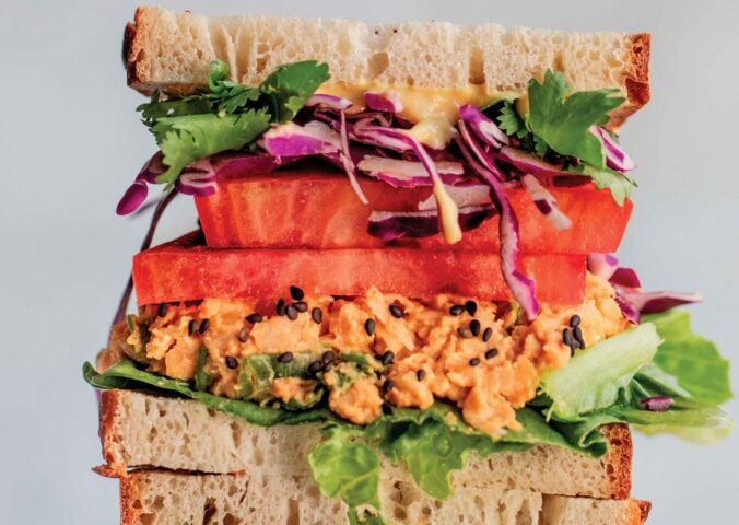 a picture of stacked peanut miso chickpea salad sandwiches with sesame, tomato, chickpea spread, and greens as part of vegan spring lunch ideas